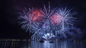 blue and red fireworks in the sky at night, over a lake