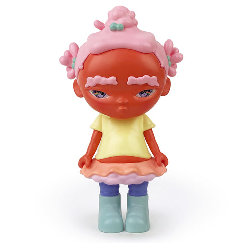 The Binky — OG figure by Rotofugi (US) showcases a representation of a Black girl with pink hair, adorned in a yellow shirt, a layered skirt of pink and orange, purple leggings, and light blue boots. Inspired by Bianca Pastel art, this figurine features a red face and maintains a neutral expression.