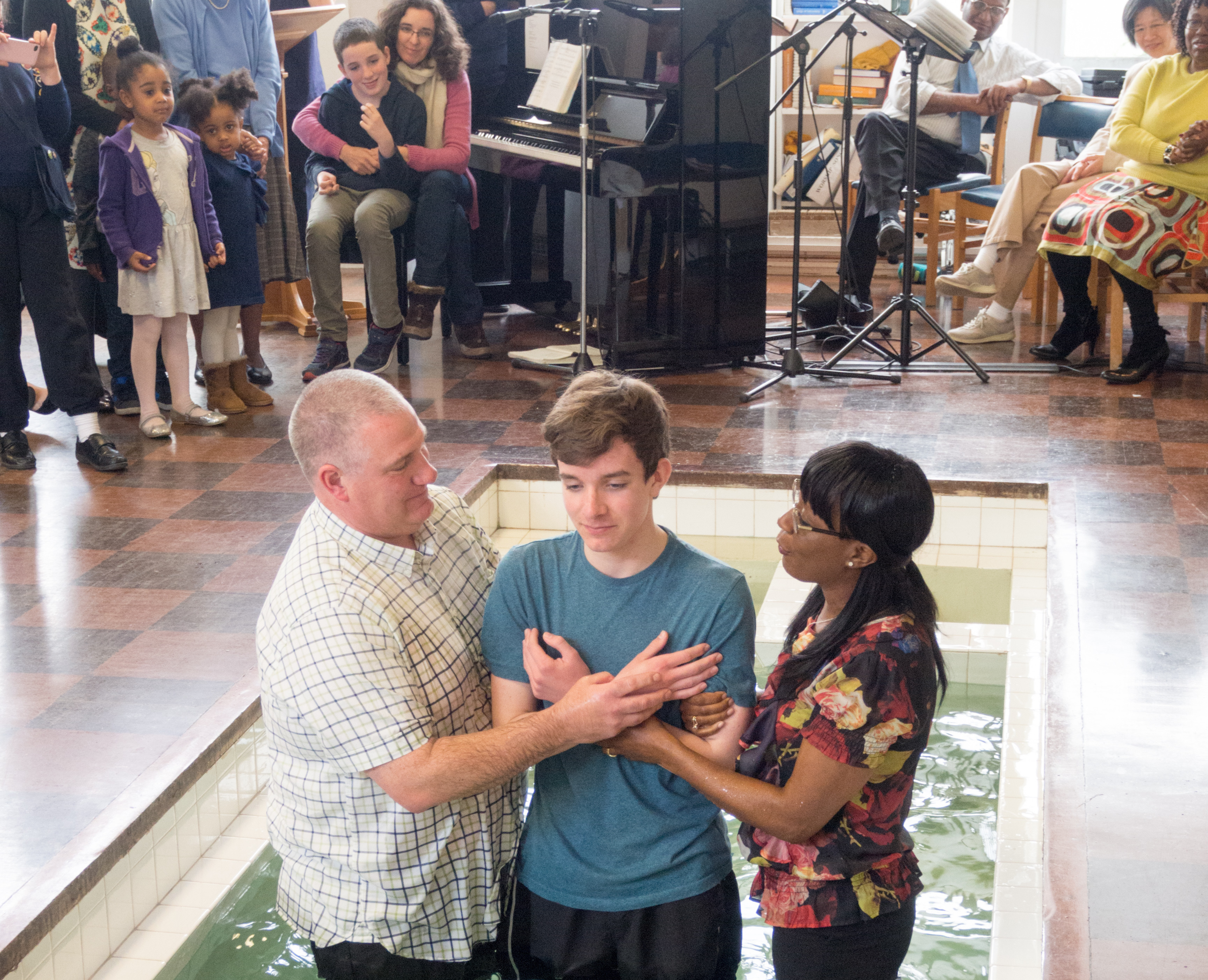 thumb Believer's baptism done by the mode of immersion, Northolt Park Baptist Church, in Greater London, Baptist Union of Great Britain, 2015, arms crossed over chest, with man and woman at either side