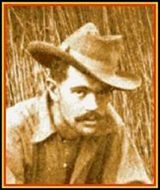 Photograph of a man wearing a wide-brimmed hat, with tall grass in the background