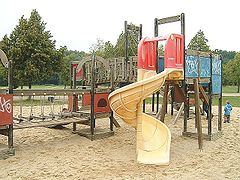 Toboggan en colimaçon au sein d'un portique de jeu, avec un parcours de jeu, lui-même intégré dans un grand bac à sable.