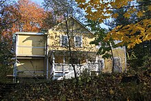 Wohnhaus mit hell gestrichener Holzfassade, mit Veranda und Treppe zum Außengelände, im ersten Stock mit Balkon.