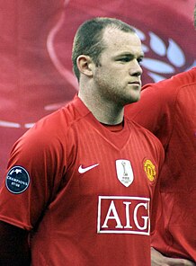 A man with short receding brown hair in a red football jersey standing before the starting of a football match.