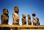 Row of six large stone statues with elongated heads on a grassy slope