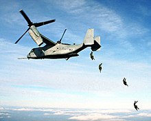 Four U. S. Marine paratroopers jump from the rear loading ramp of an MV-22 Osprey.