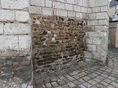 Photographie en couleurs d'un mur dont les premières assises sont en petits moellons bruns.