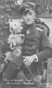 Berthold est assis, jambe croisée, regarde le photographe et tient un chien dans ses bras.