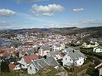 Foto von einer Anhöhe in bergiger Umgebung auf eine an einem Gewässer liegende Stadt herunter