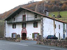 Photographie d'une large bâtisse à deux étages, avec un balcon au-dessus du premier étage.