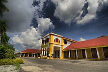 A large two storey building with two wings, painted yellow and white with a red tiled roof