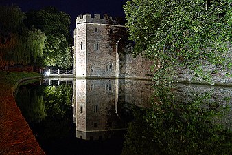 Night scene of floodlight stone walls adjoining still water.