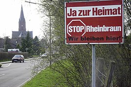 Écriteau de protestation à l’entrée du village de Holzweiler : « Oui à la terre natale — Stop Rheinbraun — Nous restons ici. ».