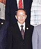 a nearly bald man, wearing glasses, a suit and a purple tie