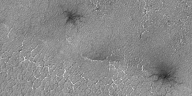 Close view of spider formations, as seen by HiRISE under HiWish program. The polygon shapes are channels caused by pressurized carbon dioxide going through cracks. During the winter season, a slab of dry ice forms on the ground surface. The surface contains cracks in the shape of polygons. During certain times, CO2 under the ice becomes pressurized from sunlight penetrating the slab of dry ice. As the gas moves around the channels become larger.