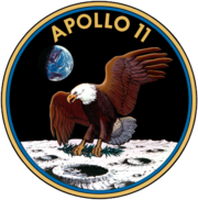 Circular insignia: eagle with wings outstretched holds olive branch on Moon with Earth in background, in blue and gold border.