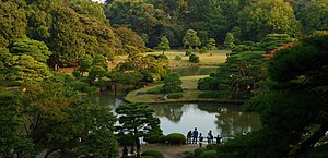 A panoramic view of Rikugi-en from Fujishiro-toge hill: green trees surround a serene lake.