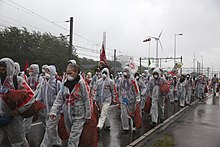 Photo of a group of people in translucent white coveralls walking down a large road.