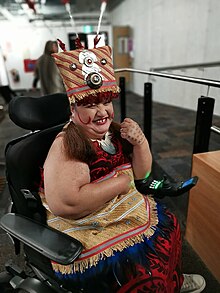 A Pacific Island woman sitting in her chair in traditional Sāmoan costume, smiling at the camera