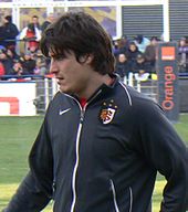 Gros plan d'un joueur à l'entraînement, vêtu d'une veste de survêtement aux couleurs du stade toulousain.