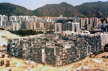 A large solid block of ramshackle buildings varying in height, with many taller buildings and some mountains in the background.