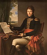 Black and white print of a man in dark military coat with gold braid and white breeches. Seated at a table, he gestures with his left hand toward a document held in his right hand.