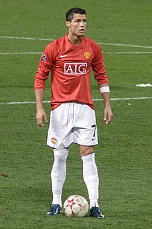 Cristiano Ronaldo – wearing a long-sleeved red jersey, white shorts with a number 7 on the left-leg side and a white armband on the left arm – prepares to take a free kick.