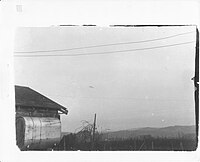 Photographie en noir et blanc d'un objet en forme de disque sur fond de ciel. Bâtiments à proximité.