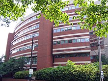 A circular, six-story brick building with decorative white concrete stripes above and below lines of adjacent square windows that encircle most of each level