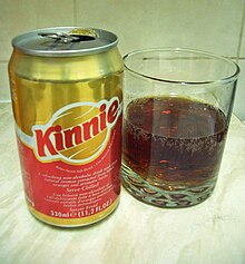 La photo couleur représente une canette de kinnie rouge en bas et or en haut. À droite, un verre présente la boisson : de couleur ambre sombre et montrant la présence de bulles, il a l'aspect d'une boisson au cola.