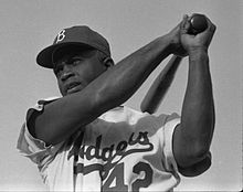 A man swings a bat; he is wearing a dark cap with a "B" on it and a jersey with the word "Dodgers" on his chest.