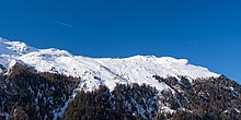 Plateau enneigé au sommet d'une montagne sur lequel se trouvent des remontées mécaniques. Plusieurs parapentes sont visibles dans le ciel.