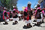 Danse du Pujllay à Tarabuco en 2010. Vue d'ensemble du costume masculin (et féminin en arrière-plan) : on distingue bien les sandales à semelle surélevée, avec leurs énormes éperons parodiques (rappelons que les premiers cavaliers du Nouveau Monde furent les conquistadors), qui servent aussi de sistres pour rythmer le pas.