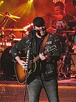 Singer Chris Young, strumming an acoustic guitar while singing into a microphone.