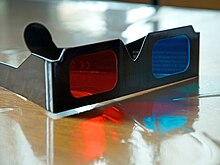 Paire de lunettes en carton noir, avec un verre de couleur bleue et l'autre de couleur rouge.