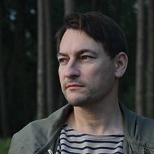 Portrait photographique en couleur d'un homme posant devant une forêt.