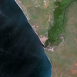 The image shows a development along the coast. To the left is a body of water. A river stretches from the settlement off to the top right corner.