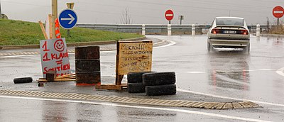 Baril, pneus et pancartes "1 klaxon = 1 soutien" et "Macron !!! Tu es un incapable, tu es licencié !" sur un rond-point.