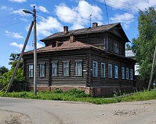 Photographie d'un immeuble en bois marron/noir à deux étages, avec l'étage moins grand que le rez-de-chaussée, et un toit en pignon.