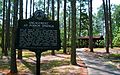 Historic marker reading "Engagement at Poison Springs" in foreground of a forested area with rustic wooden pavilion in the background.