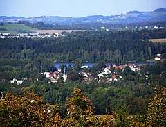 Zdjęcie wykonane ze stoku góry przedstawia górski krajobraz. Na pierwszym planie widoczne są wierzchołki drzew, za nimi, w dolinie - zabudowania wsi Baszka, za nimi znajduje się rzeka. W tle widoczne są góry o łagodnie nachylonych zboczach pokrytych lasami, łąkami i polami.