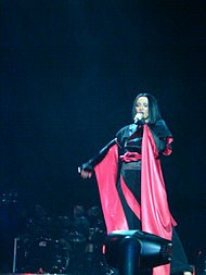 A brunette woman singing wearing a black and red kimono. Red lights and haze appear around her