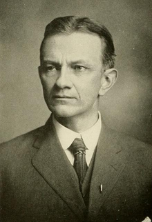 Head and shoulders photograph of a man in a Victorian suit. He has a beard, a large mustache and is slightly balding. He wears a serious expression and is looking slightly to the right.