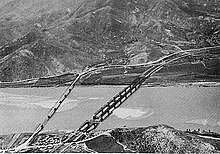 A river with two bridges extending over it, and a large hill on the south bank