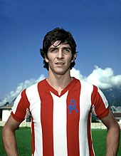 A standing man wearing a red and white sports shirt