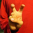 Person in orange shirt with hand in front of him with index and middle fingers crooked creating a "bent – v" shape