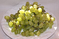 On a white plate rests a cluster of golden, green-colored Thompson Seedless grapes.