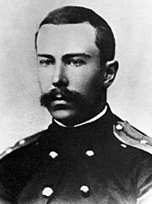 A young man with a full but neatly trimmed moustache, wearing a dark naval uniform