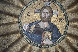 A close up photograph of a mosaic painted golden yellow, which depicts a bearded man with long hair holding a book in his left hand