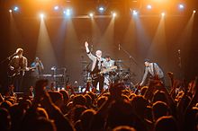 Everything Everything stand on an orange-lit stage in Kiev, Ukraine, mid-performance.