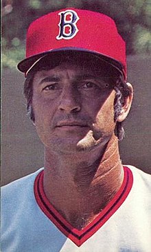 A man in a white baseball jersey and red cap